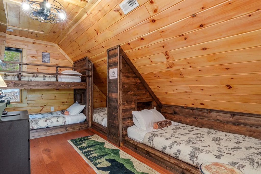 Cabin bunk room with custom twin bunks beneath the sloped pine ceiling