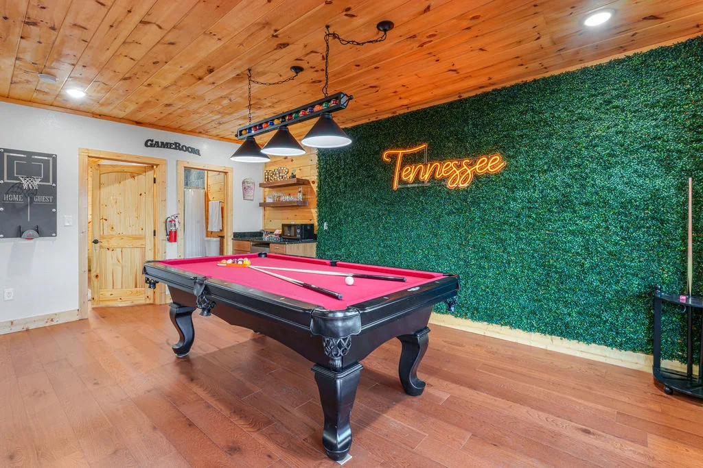 Game room with a red-felt pool table against a green accent wall lit by a neon Tennessee sign